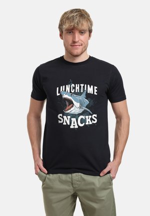 Sort bomulds-T-shirt med et grafik af en haj med åben mund og teksten "LUNCHTIME SNACKS" i fede hvide bogstaver.