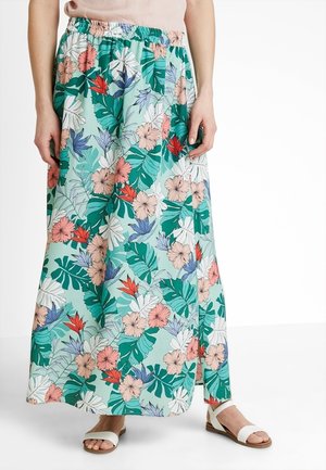 Falda maxi con cintura elástica con estampado floral tropical en verde, rosa, blanco, rojo y púrpura, usada con sandalias blancas.