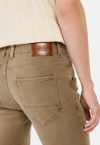 Khaki denim jeans hebben een achterpatch met het "Camel Active" logo, twee achterzakken met stikdetails en een slim-fit ontwerp.