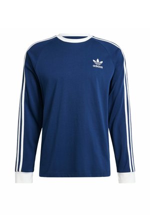 Camisa de manga larga azul con acentos blancos, con cuello redondo, puños blancos y tres rayas blancas en cada hombro. Logotipo de Adidas en el pecho.