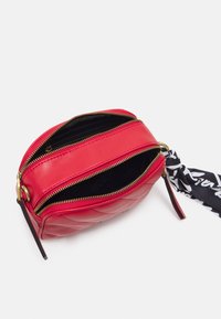 Borsa a tracolla rossa in pelle con zip dorate, motivo trapuntato, due scomparti e un'accattivante sciarpa nera e bianca.