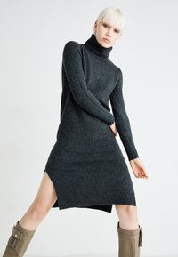Dark gray turtleneck dress with long sleeves, side slit, and ribbed hem. Styled with knee-high beige boots and smooth knit texture.