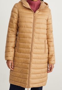 Abrigo beige acolchado con capucha, diseño acolchado vertical, cremallera frontal y bolsillos laterales. Textura suave con acabado liso.