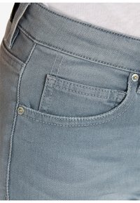 Jeans de mezclilla azul claro con un diseño clásico de cinco bolsillos, costuras sutiles y acentos de metal cerca del bolsillo frontal.