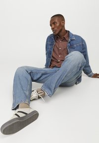 Veste en denim sur une chemise à carreaux rouges, associée à un jean léger et ample et des baskets beiges avec des rayures noires. Tenue simple et décontractée.