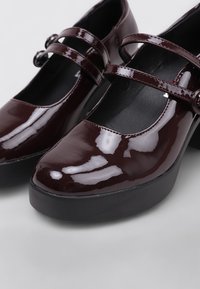 Zapatos Mary Jane de charol burdeos con diseño de doble correa, puntera redonda y una gruesa suela de plataforma negra. Acabado liso y brillante.