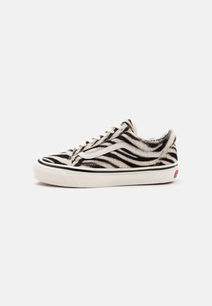 Zapatilla baja con estampado de piel de cebra en blanco y negro, suela blanca con raya negra y cordones blancos.