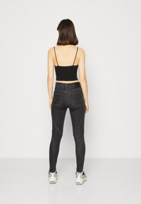 Čierny crop top s tenkými ramienkami, v kombinácii s čiernymi skinny džínami s krivkovými švami, doplnený svetlými teniskami.