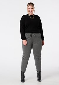 Zwarte trui met lange mouwen, grijze joggingsbroek met trekkoord en zwarte enkellaarsjes. Zachte textuur, aansluitend bij de enkels, casual ontwerp.