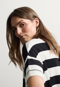Top a maniche corte a righe bianche e nere con vestibilità comoda. Tessuto morbido e scollatura a girocollo, che mostra una texture liscia e un motivo uniforme.