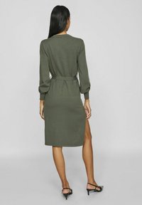 Olijfgroene gebreide jurk met lange poofmouwen, riem op de taille, knie-lengte, zijsplit, gladde structuur, minimalistisch ontwerp.