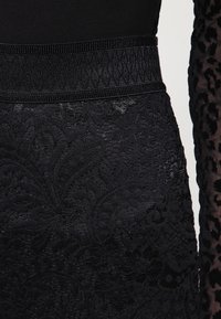 Robe noire en tissu en dentelle texturée avec des motifs floraux, une taille élastique et un corsage lisse. Les manches présentent un design en tulle avec imprimé léopard.