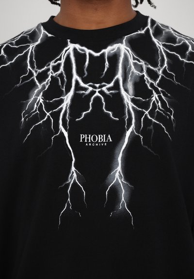 T-shirt nera con un design grafico di un fulmine bianco. Presenta il testo "PHOBIA ARCHIVE" sotto il design. Realizzata in morbido materiale di cotone.