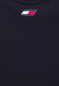 Tmavě modrá bavlněná látka s hladkým povrchem, která má v horním rohu malé logo v červené, bílé a modré barvě. Jednoduchý design.