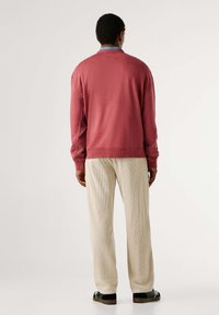 Suéter de algodón rojo con un corte relajado y puños acanalados, combinado con pantalones de pana crema que presentan una superficie texturizada. Zapatos negros completan el look.