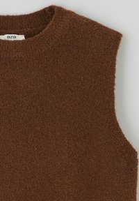 Gilet sans manches en maille brun épais avec un col rond et une petite étiquette blanche visible à l'intérieur du col.