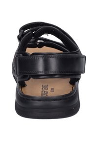 Sandalo in pelle nera con cinturini regolabili e soletta imbottita. Presenta una suola piatta e un design minimalista. Nome del marchio visibile sulla soletta.