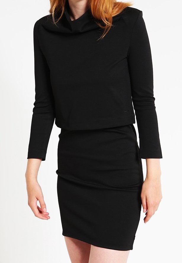 Femme portant un haut noir ajusté à manches longues et une jupe crayon taille haute assortie, sur fond blanc.