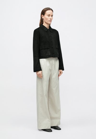 Μαύρο καφέ σουέντ κοντό σακάκι με γιακά, κουμπιά μπροστά και δύο μπροστινές τσέπες, συνδυασμένο με ανοιχτό γκρι παντελόνι φαρδύ και μαύρα �παπούτσια.