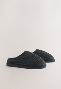 Chaussons en tissu noir tissé avec une surface texturée, bout arrondi et semelle en caoutchouc noir. Conception ouverte à l'arrière pour un style facile à enfiler.