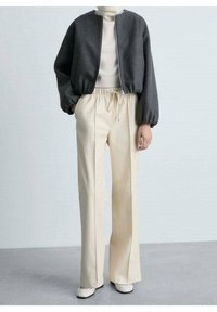 Grijze cropped jack met een ronde halslijn, gecombineerd met crèmekleurige high-waisted broek met een trekkoord. Gladde textuur, op maat gemaakte pasvorm.