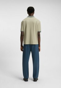 Jasnooliwkowa koszulka polo z krótkim rękawem z kontrastowym, paskowanym kołnierzykiem, zestawiona z ciemnoniebieskimi spodniami szerokimi oraz czarnym obuwiem.