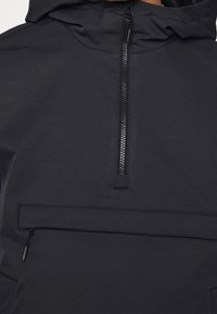 Musta huppari, jossa etupuolella puolivetoketju ja suuri vaakasuuntainen vetoketjutasku rinnassa.