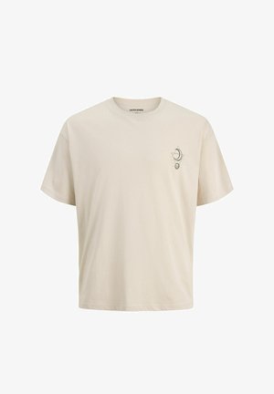 Dreng står og smiler iført en sort hættetrøje med lynlås, beige t-shirt, løse sorte bukser, beige sko og en mørkegrå baseballkasket.