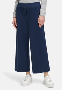 Pantaloni larghi blu navy realizzati in morbido tessuto con cintura elastica, abbinati a sneakers bianche, che mettono in mostra una silhouette elegante e moderna.