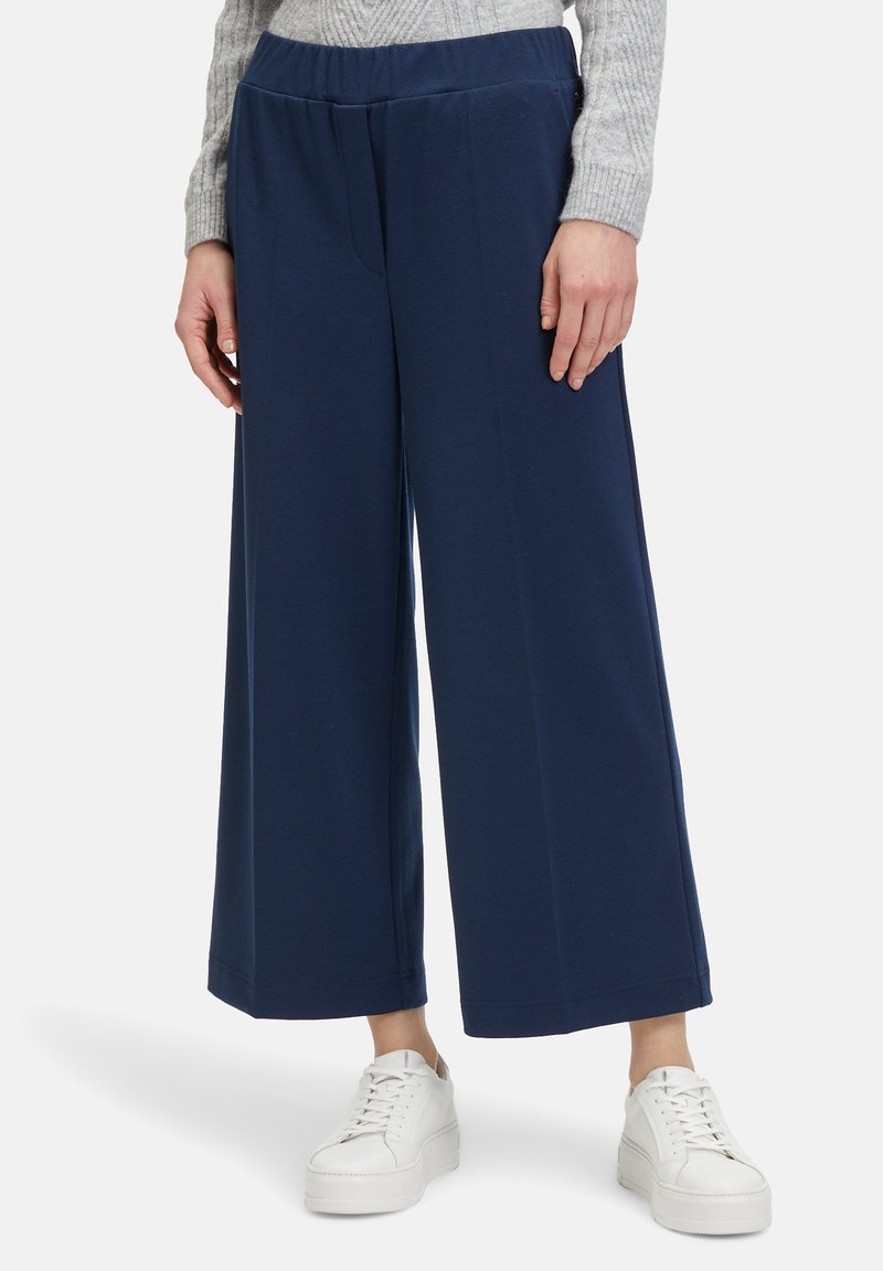 Pantaloni larghi blu navy realizzati in morbido tessuto con cintura elastica, abbinati a sneakers bianche, che mettono in mostra una silhouette elegante e moderna.