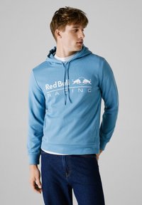 Ljusblå huvtröja i mjuk väv med en framficka i kangaroo-stil. Har en vit "Red Bull Racing"-logotyp över bröstet.