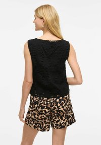 Black knitted top with floral patterns, rounded neckline, and sleeveless design, paired with tan and black leopard-print shorts.