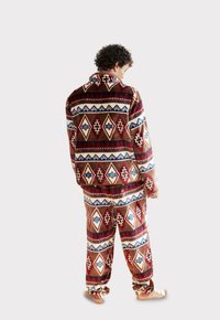 Zestaw piżamowy z polarowego materiału z geometrycznym wzorem w kolorach czerwonym, brązowym, białym i niebieskim. Zawiera długi rękaw top oraz dopasowane spodnie z elastycznymi mankietami.