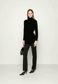 Fekete garbó pulóver hosszú ujjakkal és oldalt megkötve, csíkos szövetnadrággal párosítva. A megjelenést fekete magassarkú cipő és kézitáska teszi teljessé.