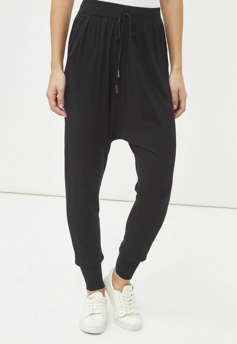 Pantalones harem negros confeccionados con una tela suave, que cuentan con una cintura con cordón, puños ajustados y bolsillos laterales para mayor comodidad.