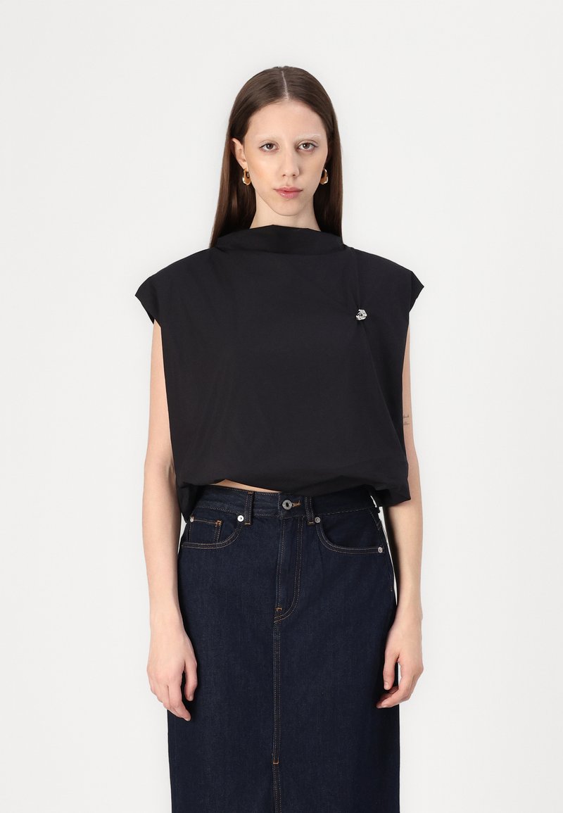 Top nero a maniche corte con colletto alto e dettaglio di spilla decorativa; indossato con una gonna di jeans scura caratterizzata da cuciture in evidenza.