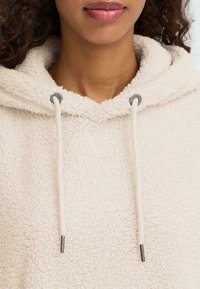 Béžová fleecová mikina s měkkým, texturovaným povrchem, šňůrkami s kovovými konci a kulatým výstřihem.