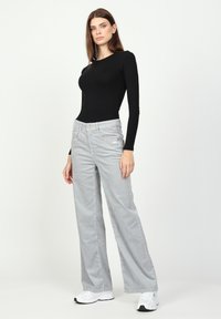 Schwarzes Langarmoberteil kombiniert mit grauen weiten Cordhosen und weißen Sneakers. Das Outfit hat ein figurbetontes Design und eine subtile Textur.