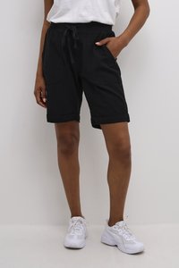 Shorts noirs en coton, arrivant au genou, avec une taille à cordon de serrage, des poches à l'avant et des ourlets roulés, associés à des chaussures de sport blanches.
