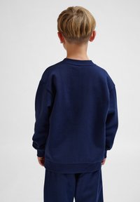 Marinblå sweatshirt i mjuk bomull, med rundad halsringning, sänkt axel och ribbade mudd- och nederkanter, bärs med matchande byxor.