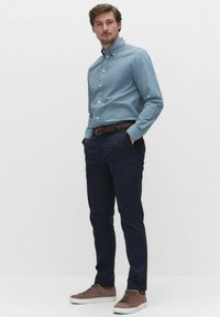 Lyseblå skjorte med knap, mørk navy bukser, brune sneakers. Skjorten har en krave, og outfittet inkluderer et vævet brunt bælte.
