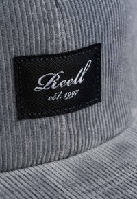 Gray corduroy cap featuring a black patch with "Keell" and "est. 1997" embroidered in white cursive text. Textured fabric is visible.