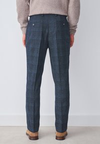 Pantalones de cuadros azul marino con una tela texturizada, que cuentan con dos bolsillos traseros y un ajuste entallado. Combinados con zapatos de ante marrón.