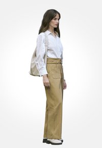 Lekko pasekowana koszula na guziki, beżowa torba płócienna, spodnie khaki z wysokim stanem i białe buty z czarną podeszwą.