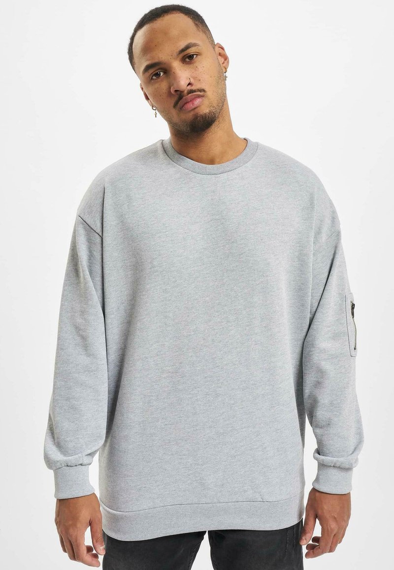 Grauer Sweatshirt mit langen, lockeren Ärmeln, gerippten Bündchen und einer seitlichen Reißverschlusstasche. Hergestellt aus weichem Material, mit rundem Halsausschnitt und lockerer Passform.