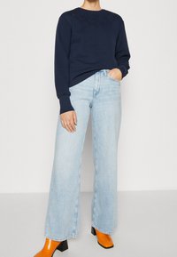 Felpa navy con ricamo floreale sul petto, abbinata a jeans a gamba larga azzurri e stivaletti con tacco arancioni vivaci.