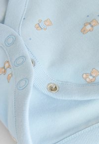 helehelesinine puuvillane bodi, millel korduv karumustri disain, ümarad pükstega klõpsud ja soonikkoeline kaelus, sileda tekstuuri ja minimaalsete dekoratiivsete elementidega.