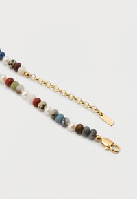 Χρυσό κούμπωμα αστακού και αλυσίδα προσαρτημένα σε βραχιόλι με ανάμεικτες στρογγυλές πολύχρωμες πέτρες και λευκές πέρλες σε λευκό φόντο.