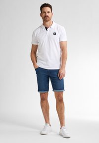Bílé polo tričko s černými detaily na límci, skombinované s modrými denimovými šortkami a bílými teniskami. Jednoduchý design, krátké rukávy a ohrnuté lemové šortky.