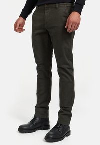Pantalones tapered de color verde oscuro, confeccionados con una tela texturada, que cuentan con un cierre de botón y bolsillos laterales, combinados con botas negras hasta el tobillo.